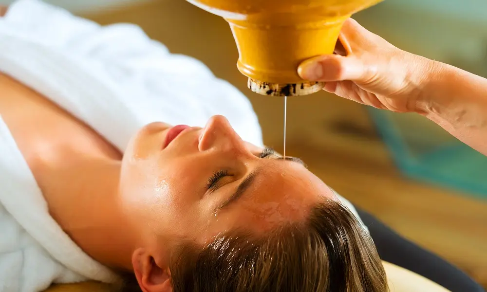 Warm oil poured onto the forehead during a Shirodhara therapy session
